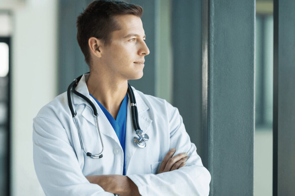 Surgeon gazing out a hospital window, contemplating long-term purpose and the freedom passive income can provide.