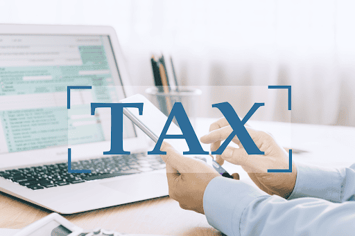 A tax banner overlaps a blurred computer and a man’s hands, holding a smartphone
