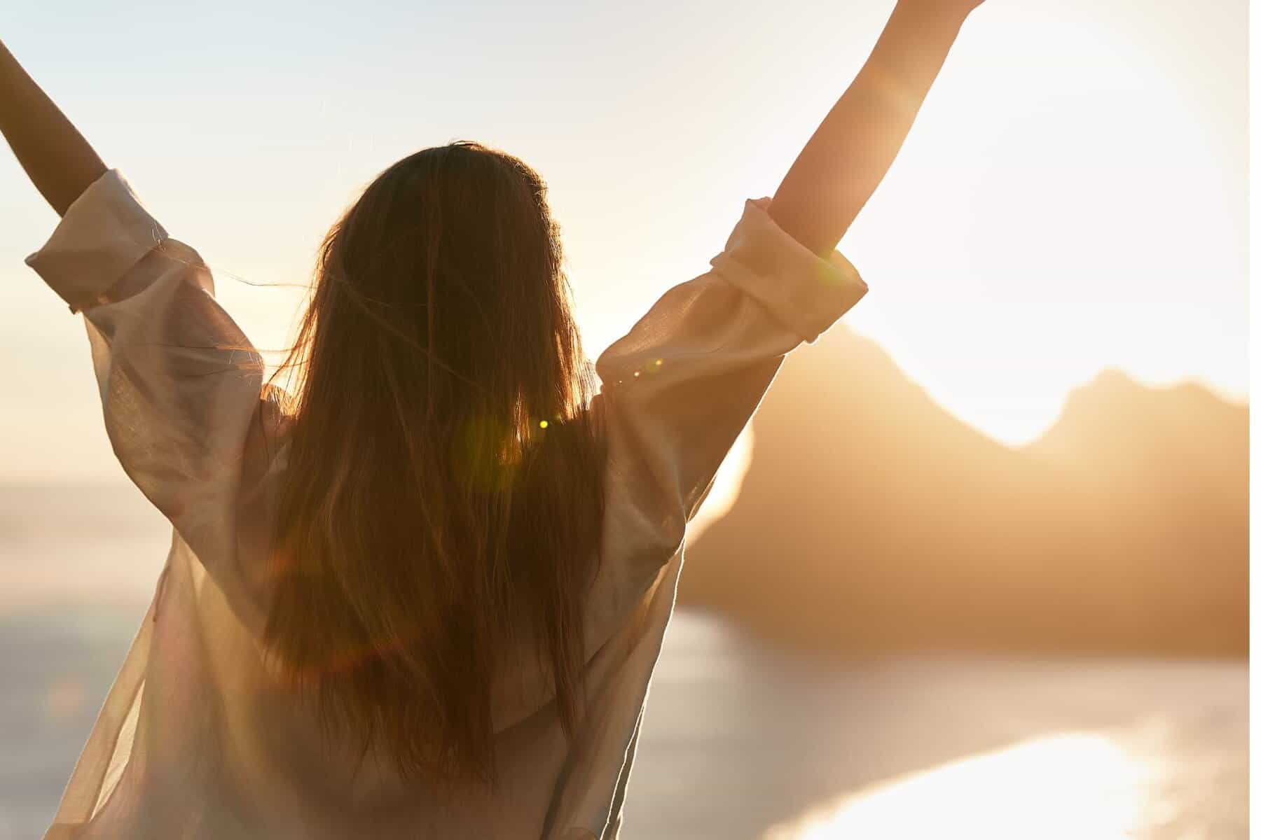 Woman stands with her arms raised, facing the scenery