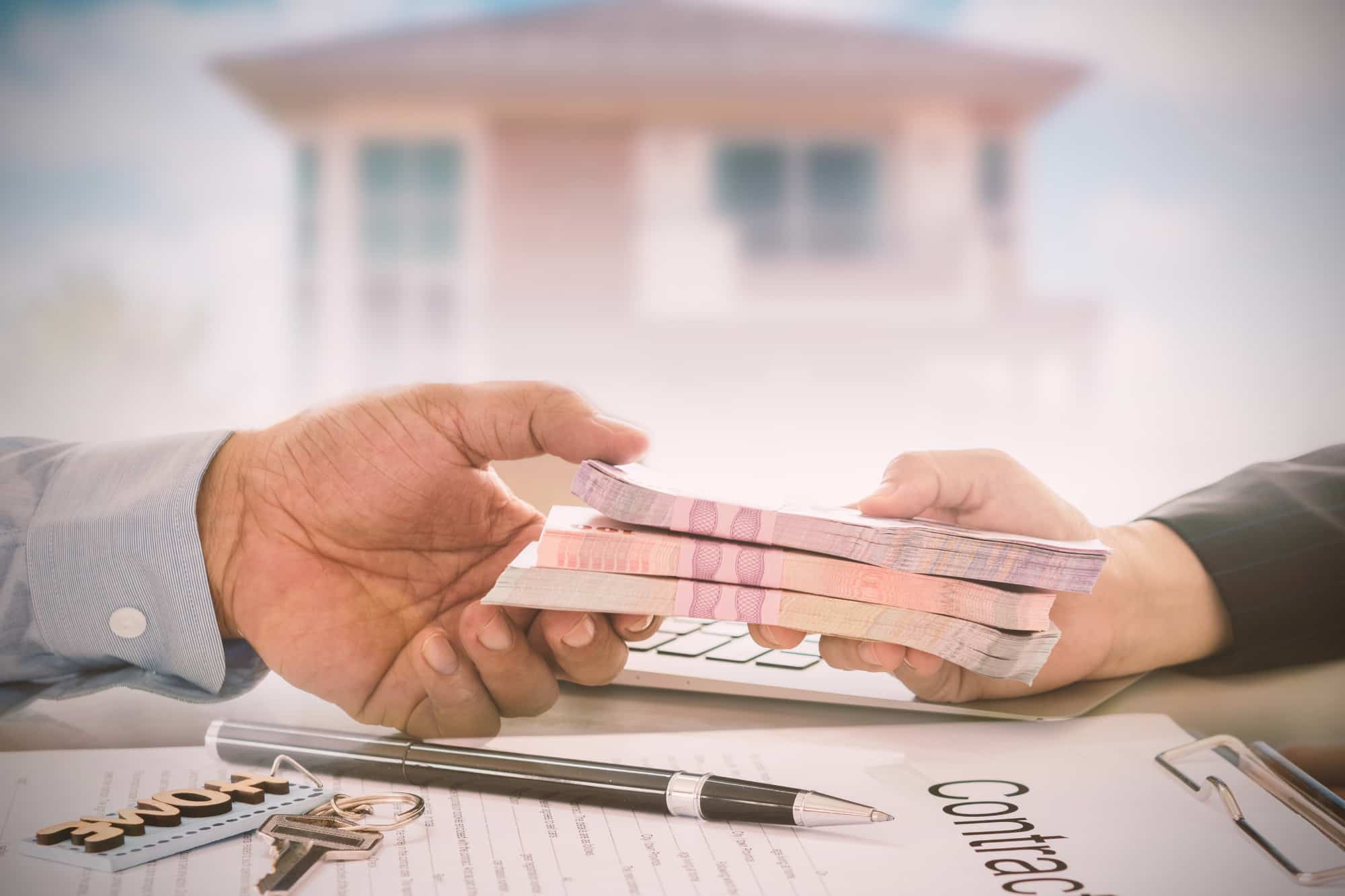 A person is handing over a stack of money for a house, representing physician loans and real estate contracts.