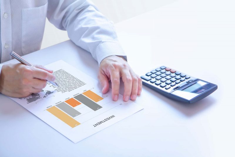 A man with a pen reviews an “Investment” document, and a calculator sits next to the man