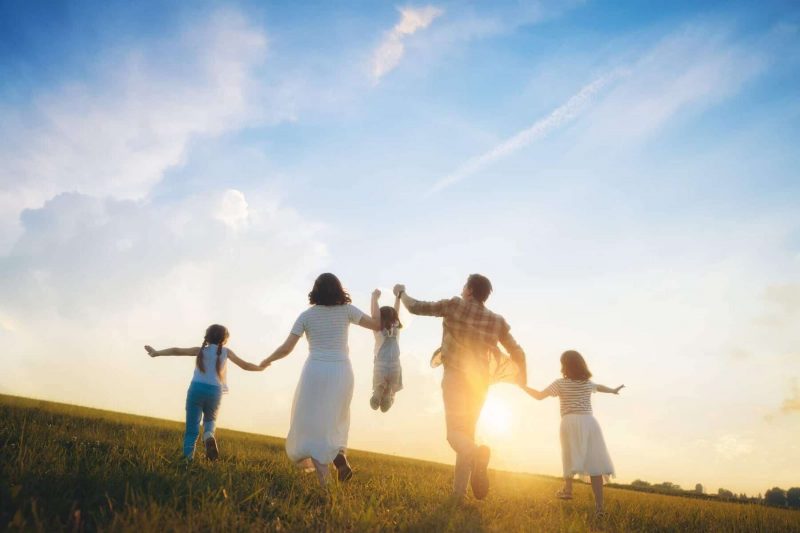 A family of five walks hand-in-hand in a meadow