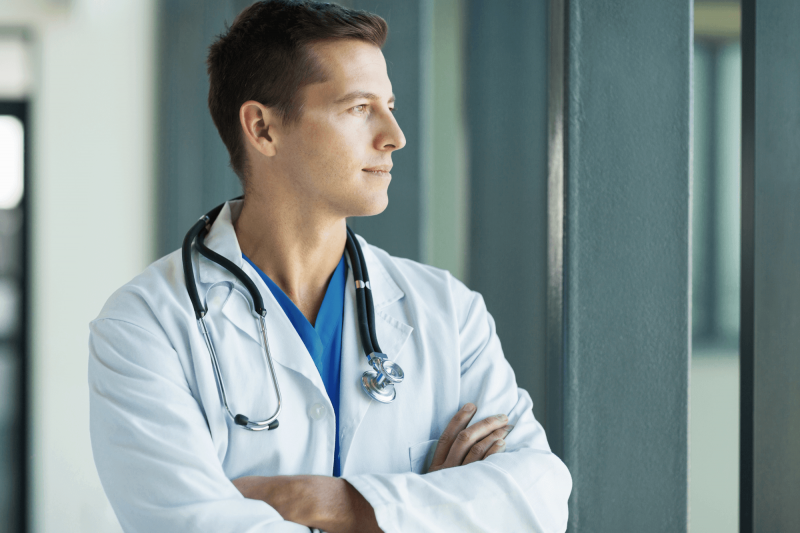 Surgeon gazing out a hospital window, contemplating long-term purpose and the freedom passive income can provide.