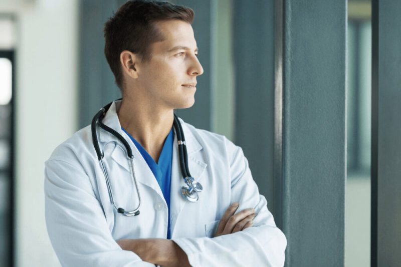 How To Invest In Real Estate For Passive Income As Surgeons – 3 Surgeon gazing out a hospital window, contemplating long-term purpose and the freedom passive income can provide.
